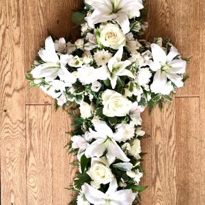 An elegant open cross tribute in all white with lush foliage. Flower colour of your choice. 24 hours notice. Due to seasonal variations some items may be substituted to produce a display of equal quality and value. Professionally arranged by our expert florists with care. Delivered by hand by our own driver. Click & collect is also available